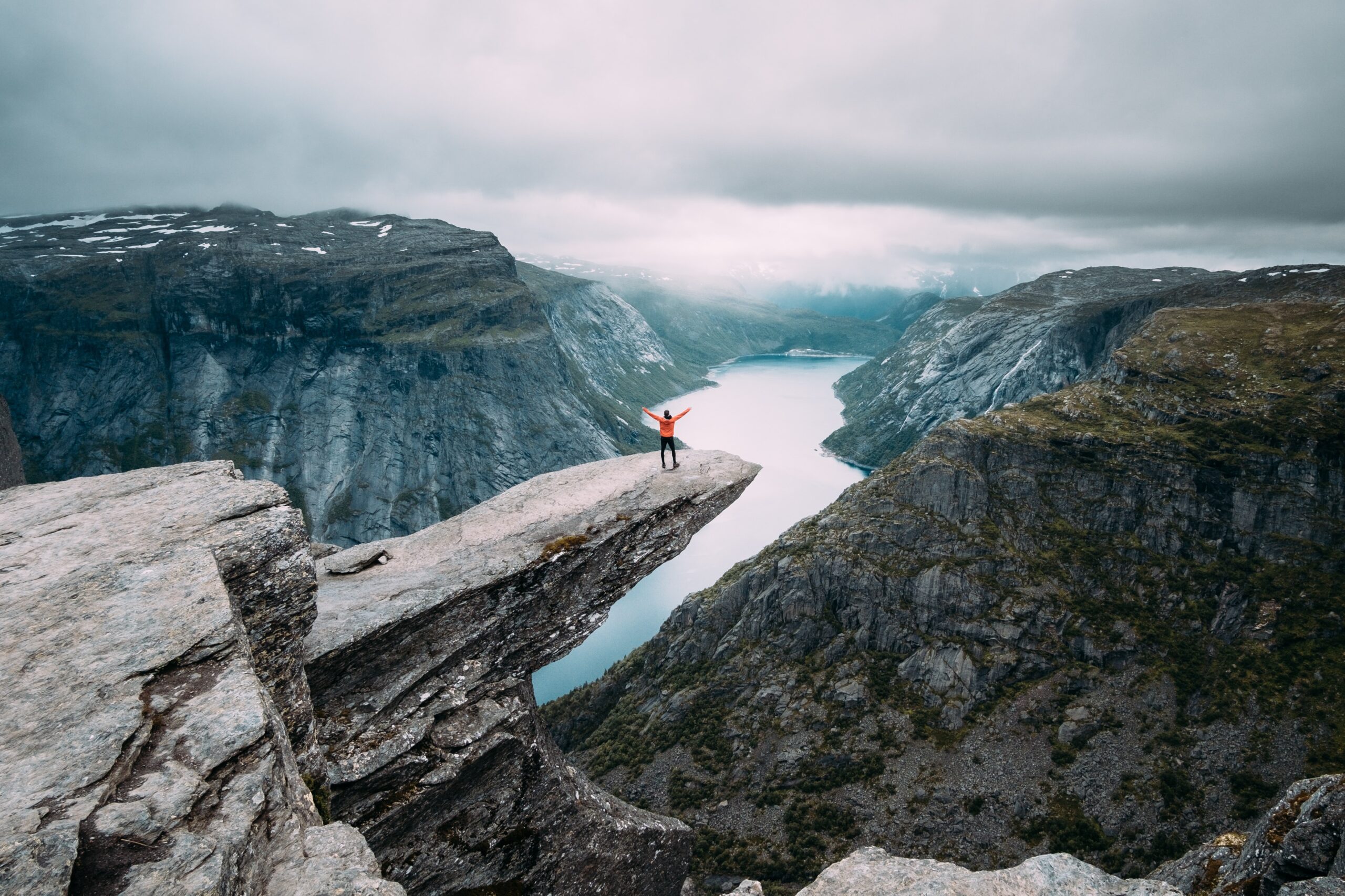 A Person With Hands Raised Standing at the Edge of a Cliff Infront of Snowcapped Mountain