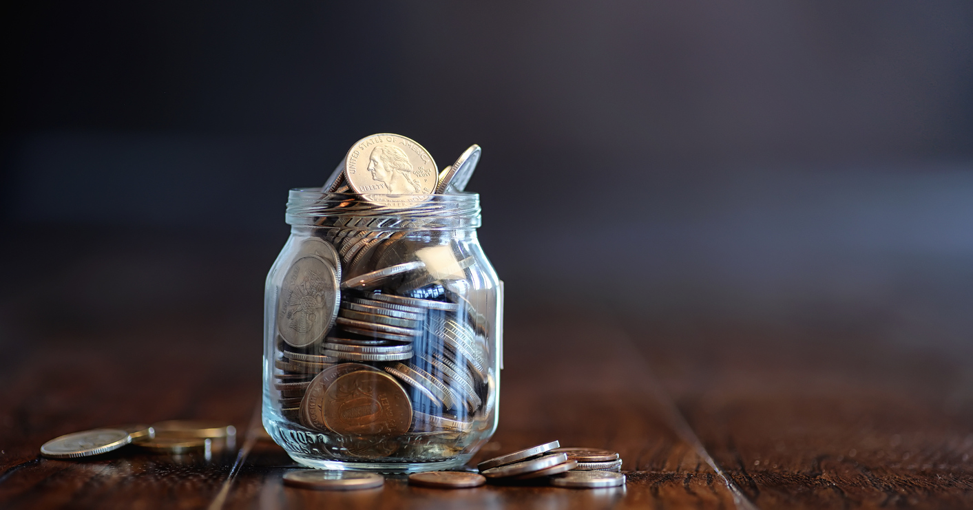 Coins in a Glass Jar on a Wooden Floor.