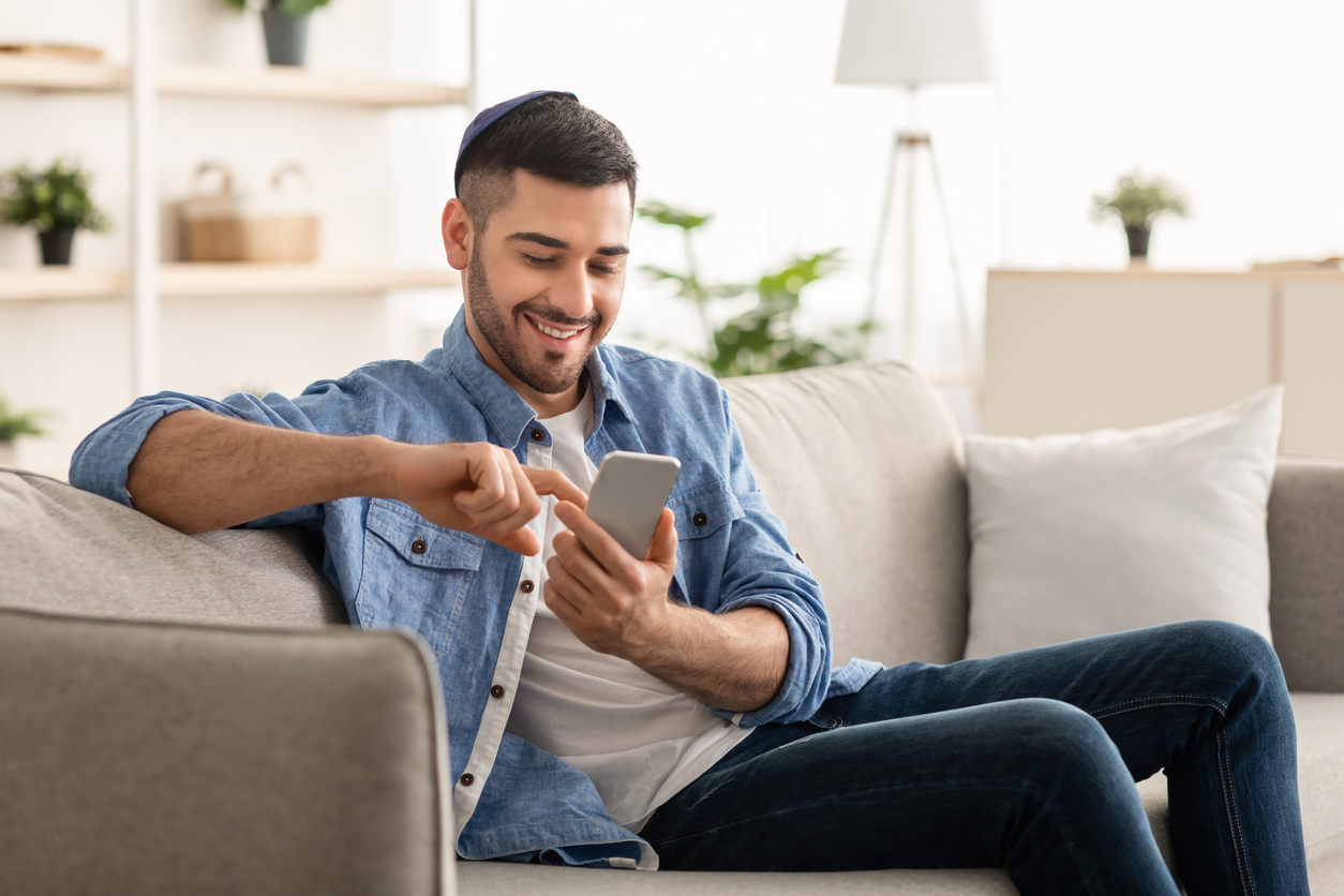 Smiling jew man using smart phone sitting on couch