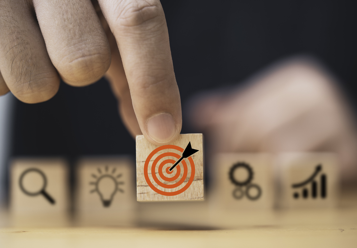 Hand putting target board which printing on wooden cube block on mechanical gear and lightbulb icon for creative and set up business objective target goal concept.